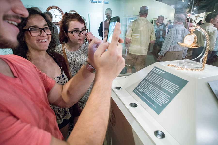 onlookers inspecting a pocketwatch through glass case